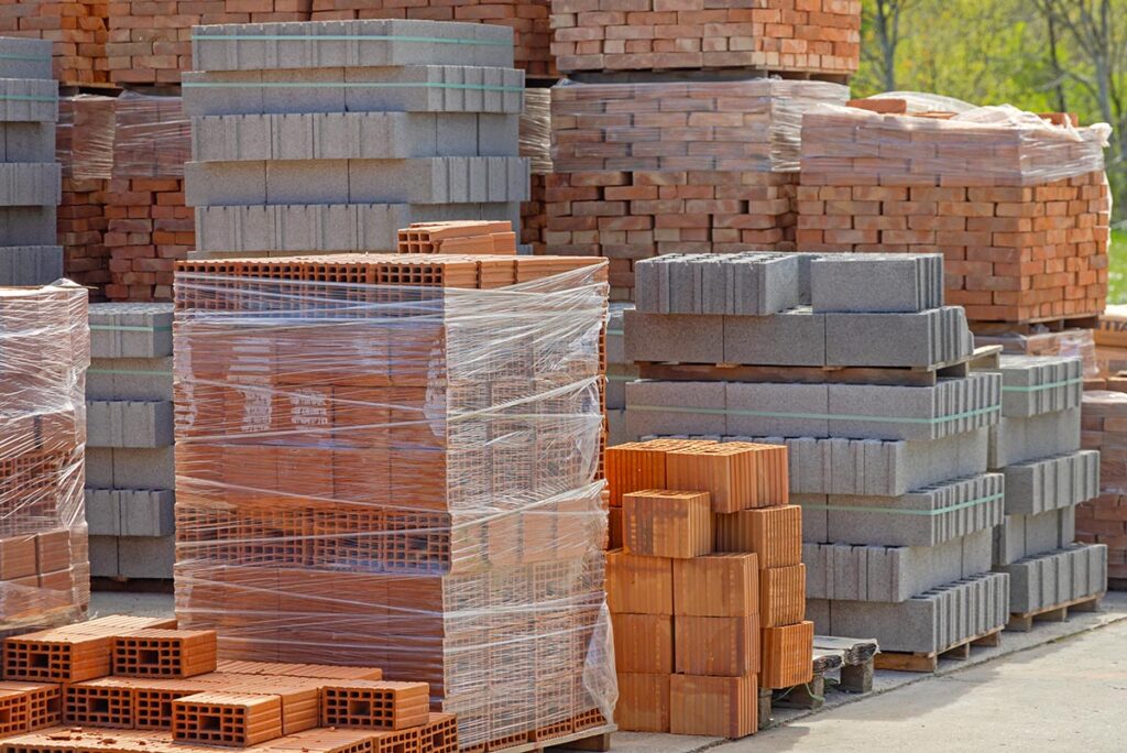Stacks of bricks and concrete blocks on pallets at a construction materials yard.