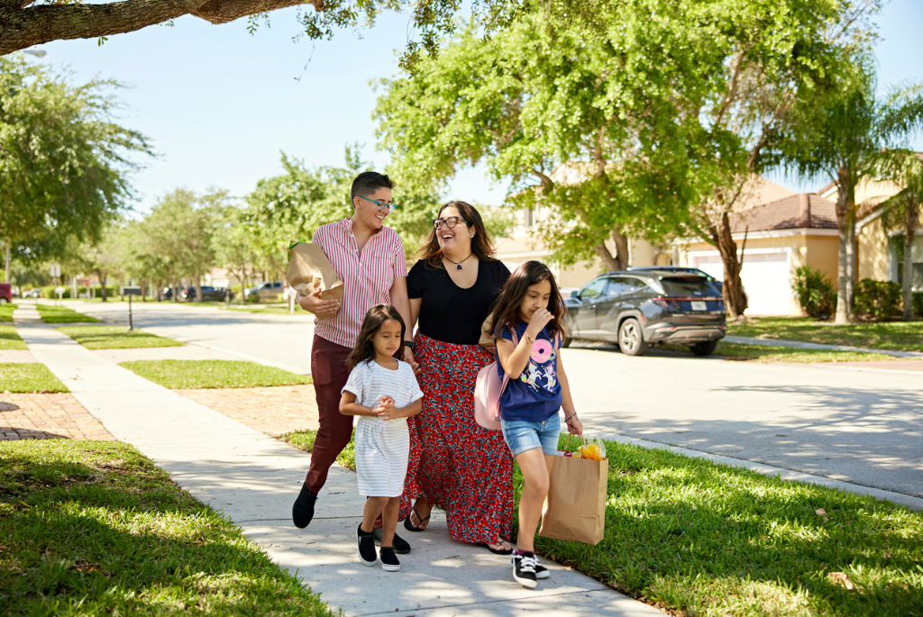 Family walking through a tree-lined suburban neighborhood with nearby homes and amenities, illustrating a walkable 15-minute suburb.