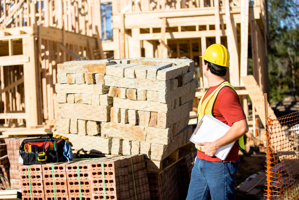 Construction supervisor reviewing stacked masonry materials on-site to manage inventory and prevent delays in a single-family home project.