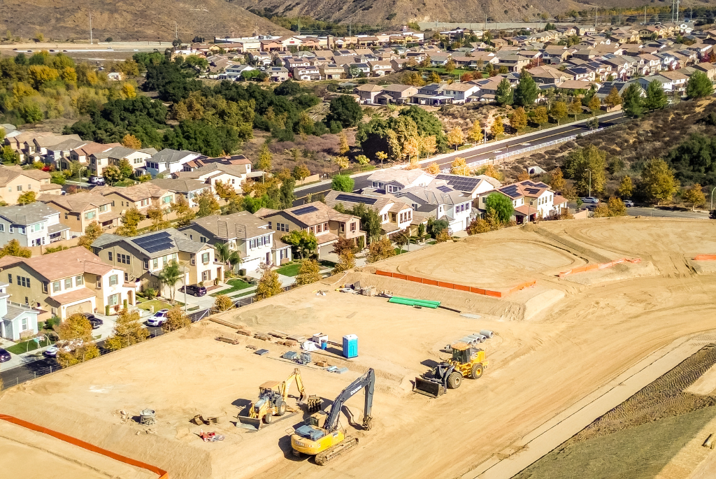 Aerial view of a residential development site with active grading work and heavy equipment near completed homes.