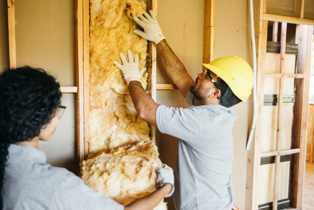 Construction workers installing wall insulation inside a wood-framed residential building during an energy-efficiency upgrade.