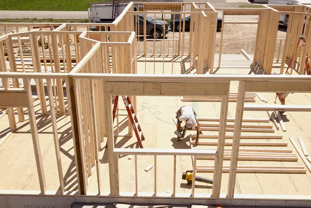 Residential home framing under construction with workers assembling interior walls and floor plan layout on a new build site.