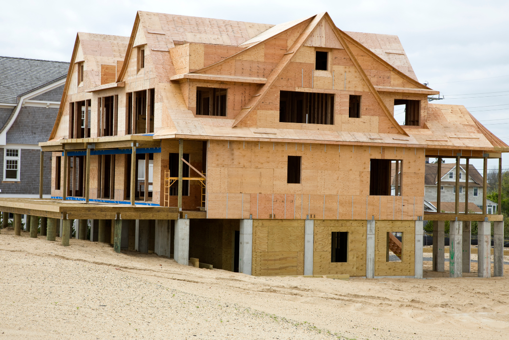 Large elevated coastal home under construction with reinforced framing and foundation supports designed for extreme weather resilience.